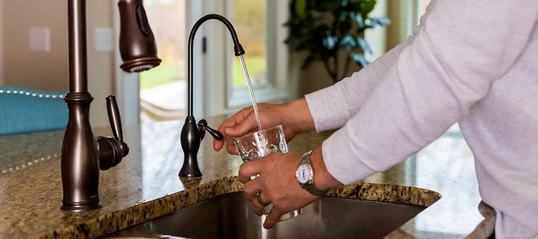 man pouring a glass of water from an RO system