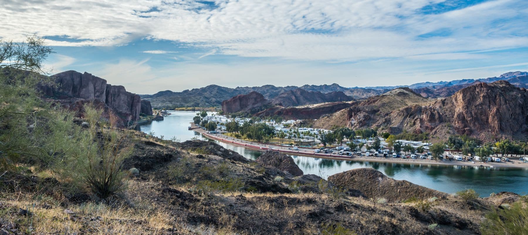 A scenic view of Parker, Arizona, featuring a winding river, rugged mountains, and a peaceful RV park along the shoreline