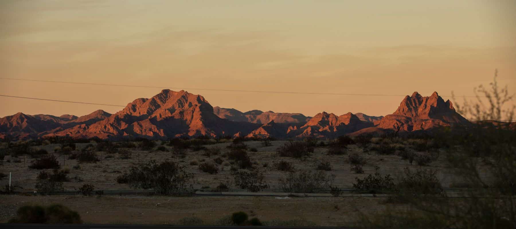 A vast desert landscape with rugged mountain peaks bathed in warm golden light during sunset
