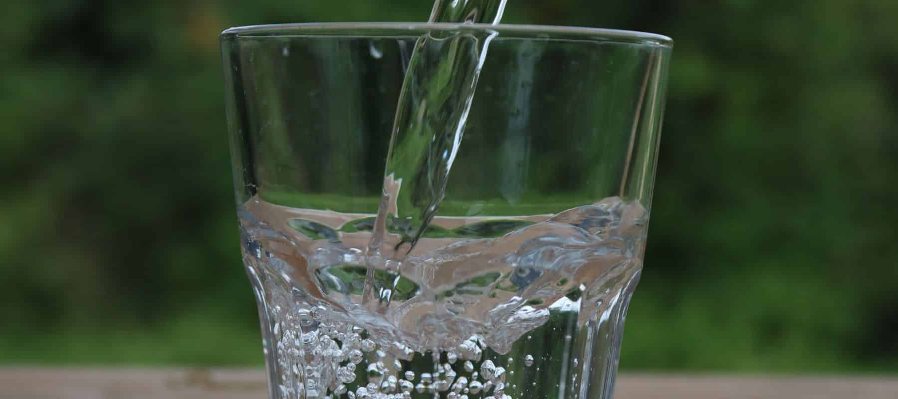 glass cup being filled up with water in front o fa green scenery backdrop