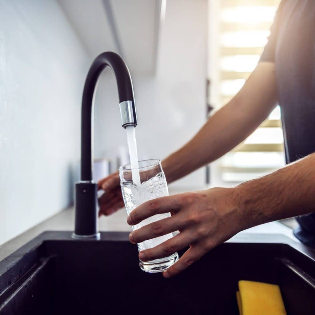 Person filling a clear glass with water from a modern kitchen faucet