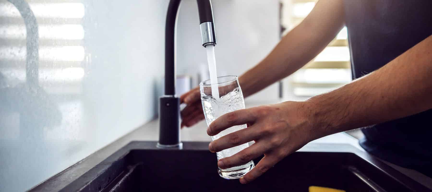 Person filling a clear glass with water from a modern kitchen faucet