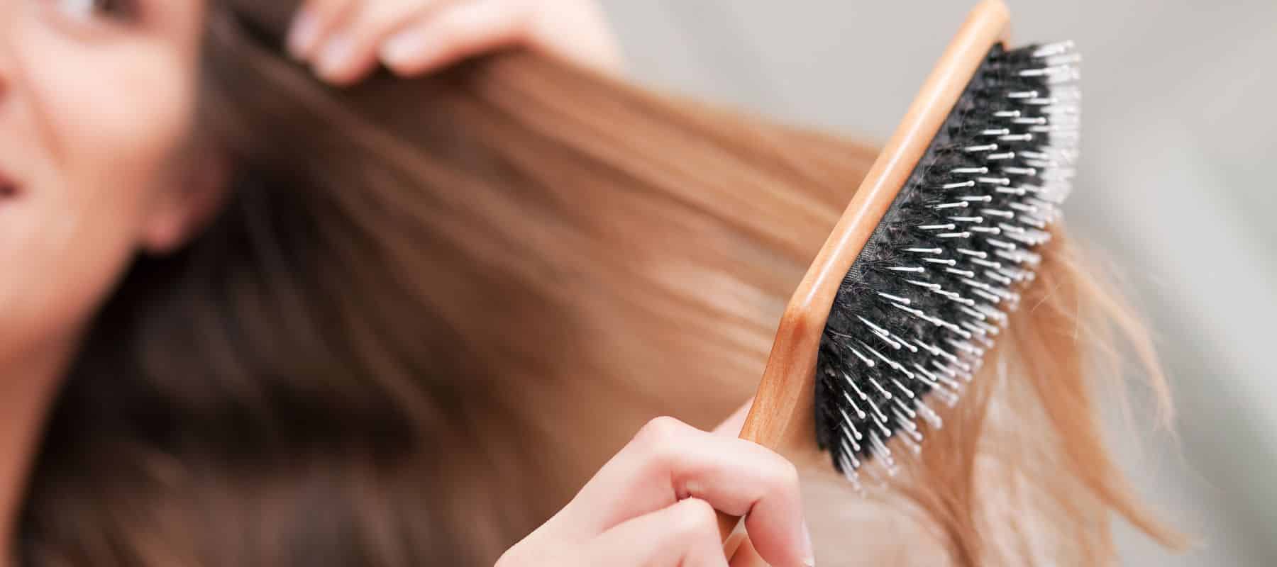 closeup of a woman brushing her hair with a brush thats getting stuck in it