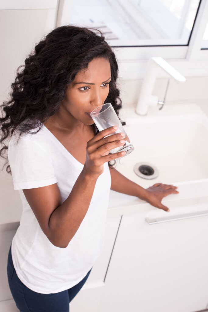 Woman drinking water at sink.